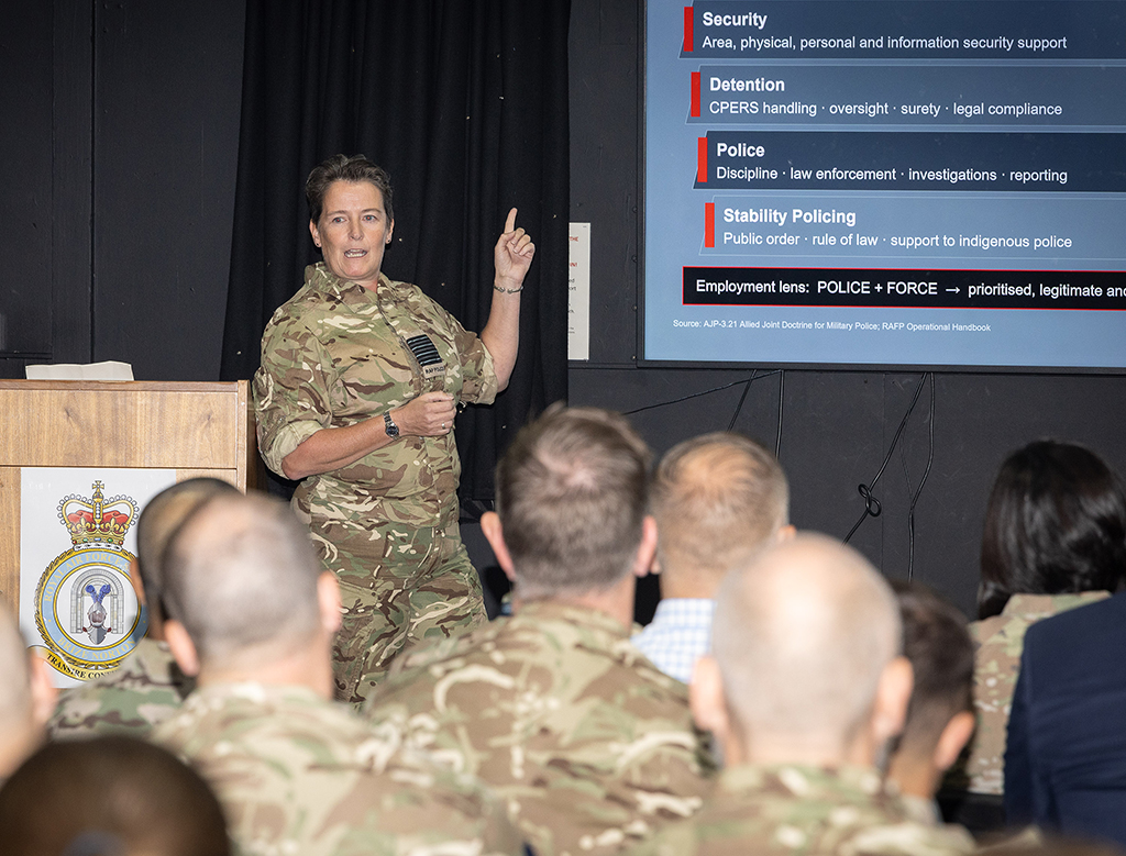 Group Captain Samantha Bunn PM (RAF)/Commander RAF Police Force addresses the gathered audience from a dias on a stage.